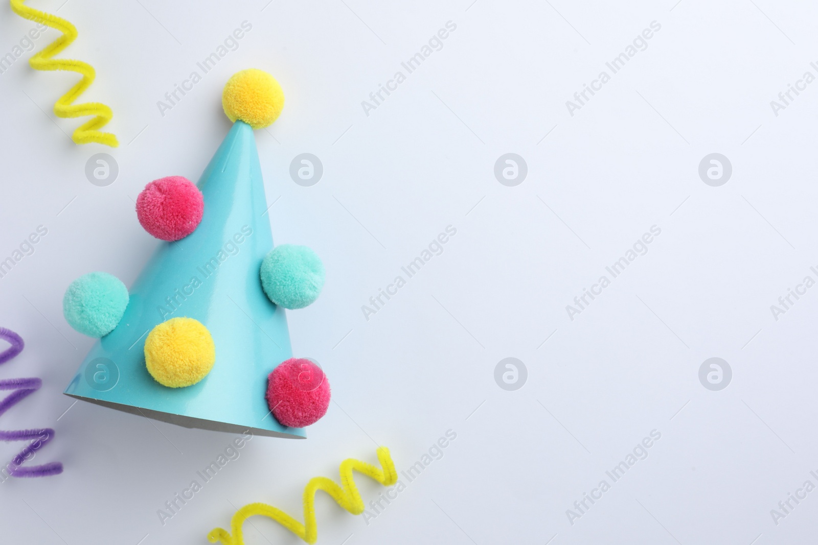 Photo of One blue party hat with pompoms on light background, top view. Space for text