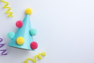 One blue party hat with pompoms on light background, top view. Space for text