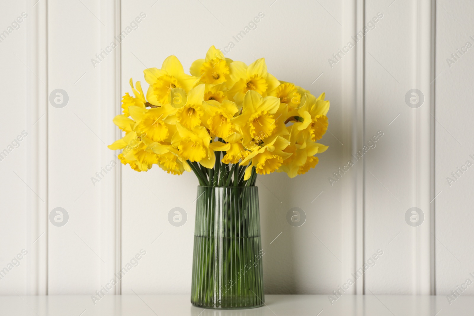 Photo of Beautiful daffodils in vase on table near white wall indoors