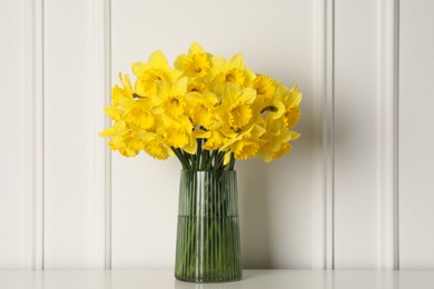 Beautiful daffodils in vase on table near white wall indoors