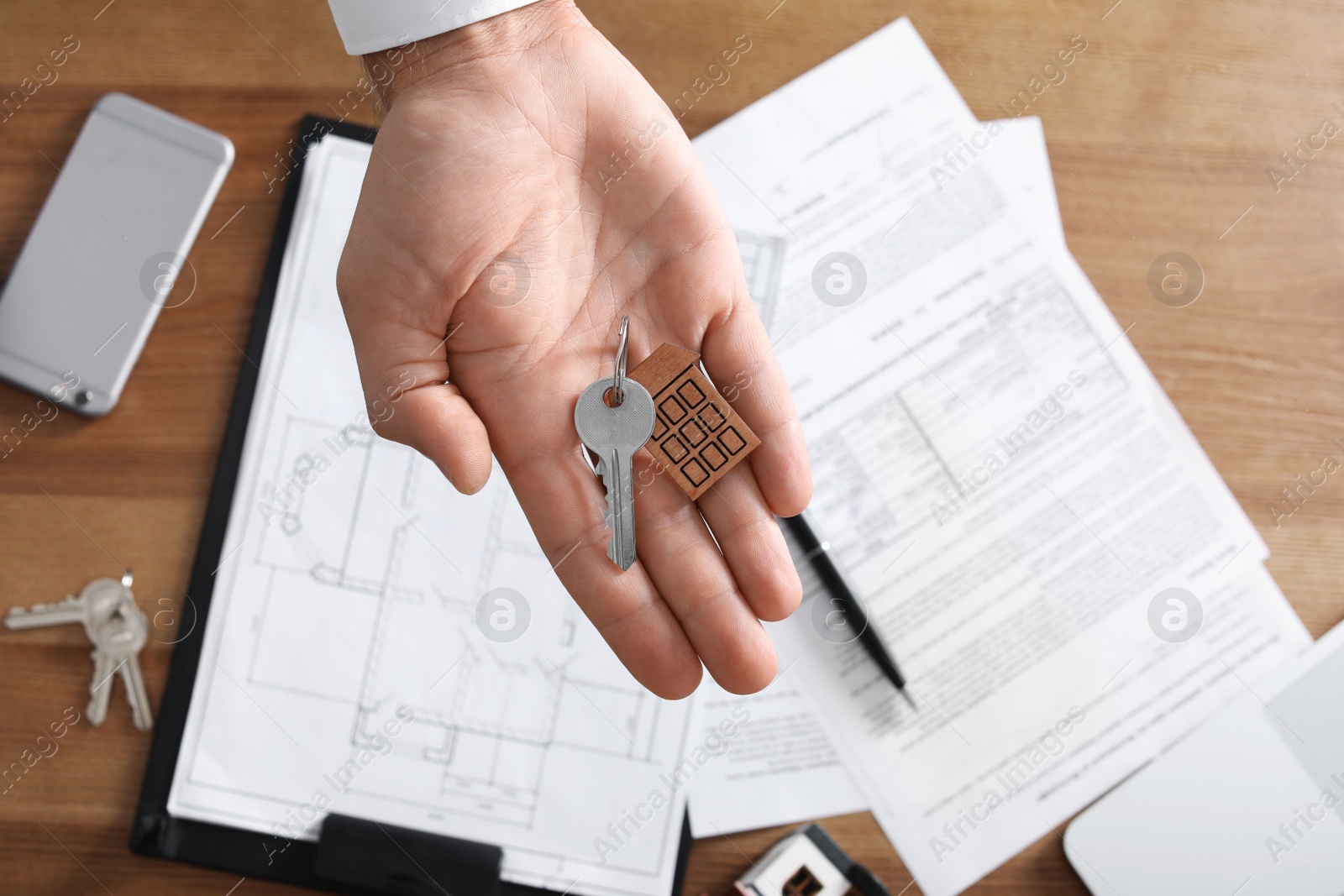Photo of Real estate agent holding key over table in office, top view