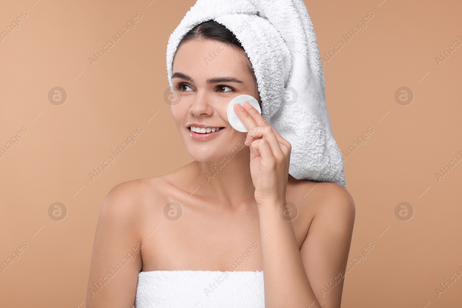 Photo of Young woman cleaning her face with cotton pad on beige background