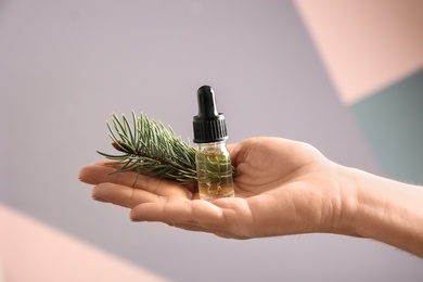 Photo of Woman holding bottle of essential oil and fir branch on color background, closeup