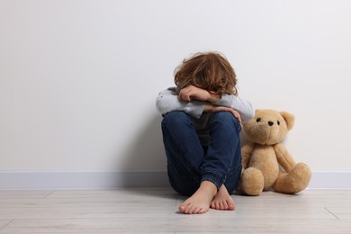 Photo of Child abuse. Upset boy with toy sitting on floor near white wall, space for text