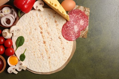 Pizza base and products on green textured table, flat lay. Space for text