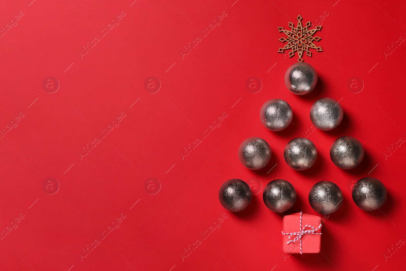 Photo of Christmas tree shape made of festive decorations and gift box on red background, flat lay. Space for text