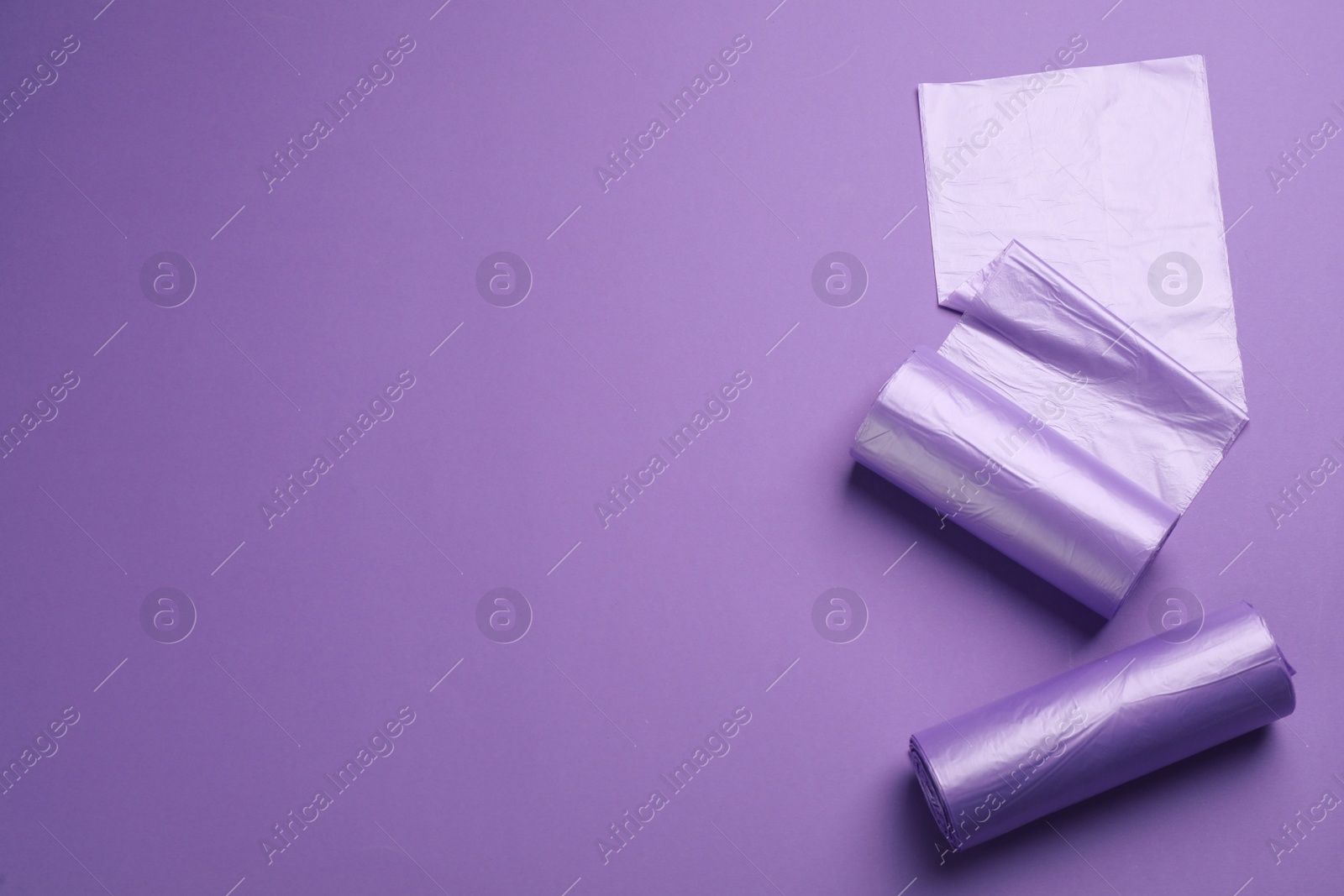 Photo of Rolls of color garbage bags on violet background, flat lay. Space for text