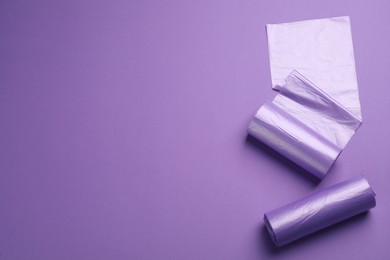 Photo of Rolls of color garbage bags on violet background, flat lay. Space for text