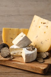 Photo of Board with delicious cheeses and fresh black truffles on wooden table