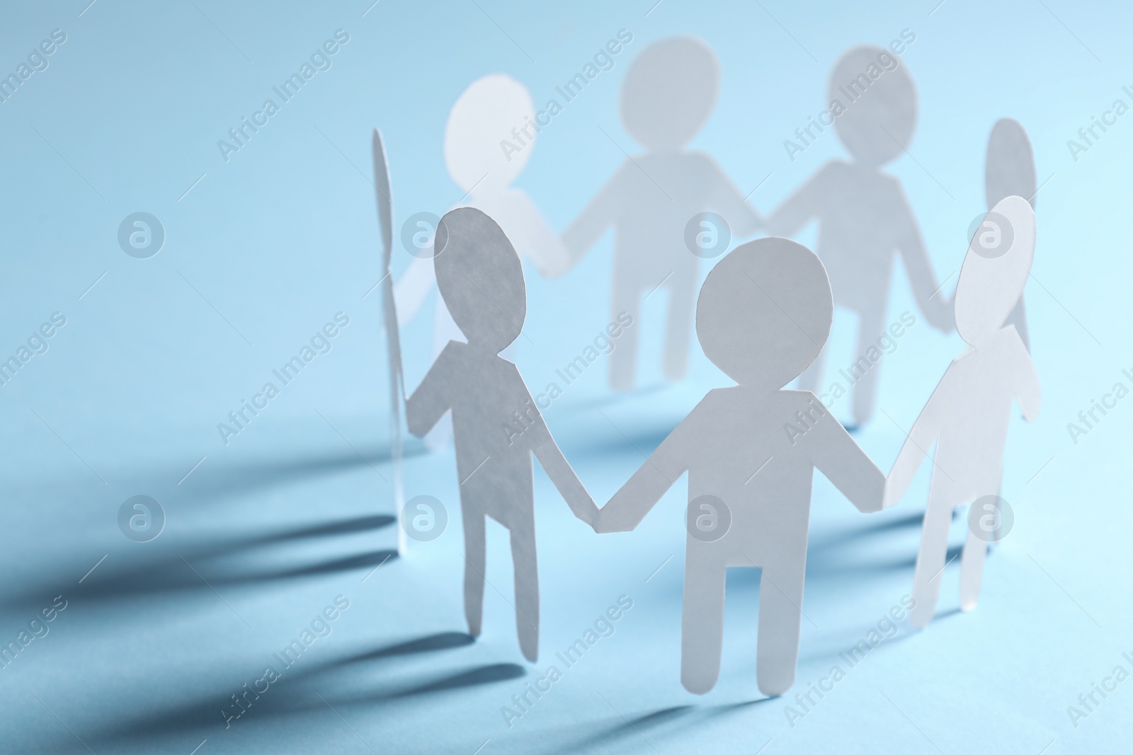 Photo of Teamwork concept. Paper figures of people holding hands on light blue background, closeup and space for text