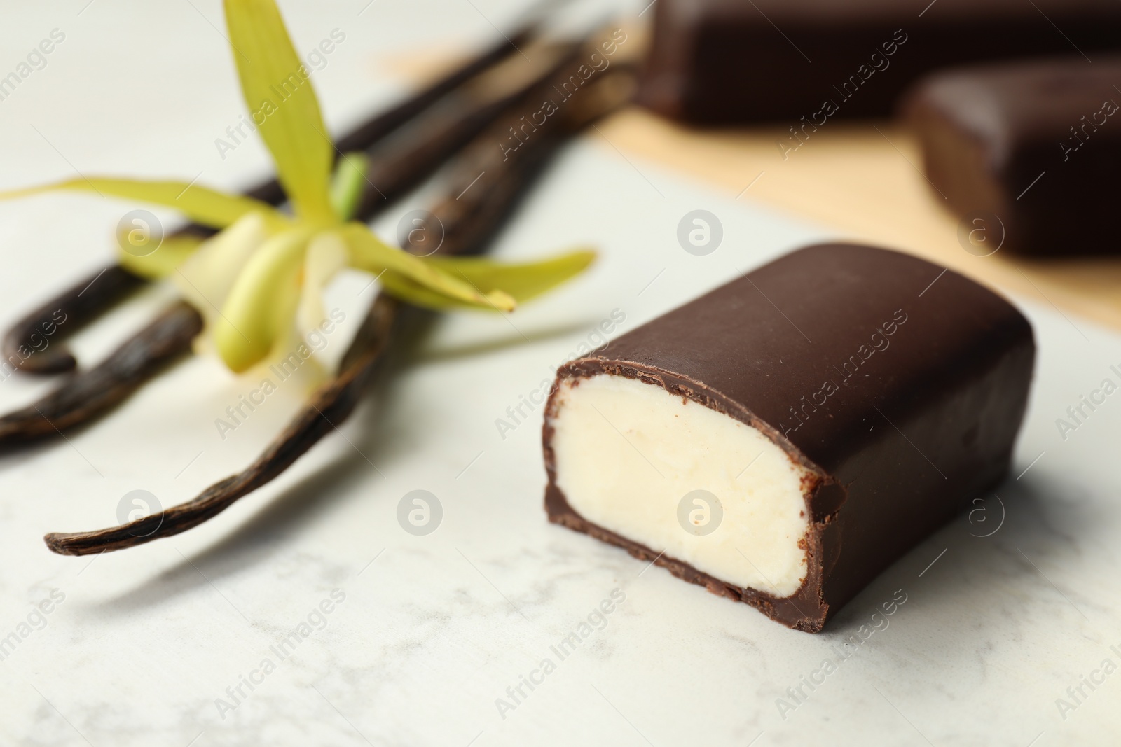 Photo of Glazed curd cheese bars, vanilla pods and flower on white table, closeup