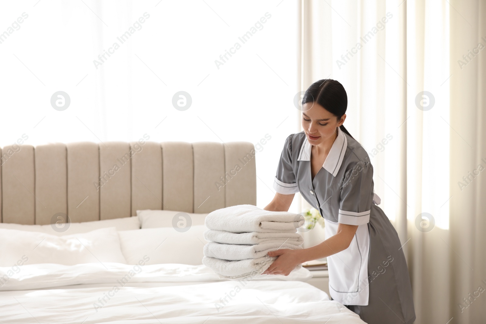 Photo of Young chambermaid putting stack of fresh towels in bedroom. Space for text