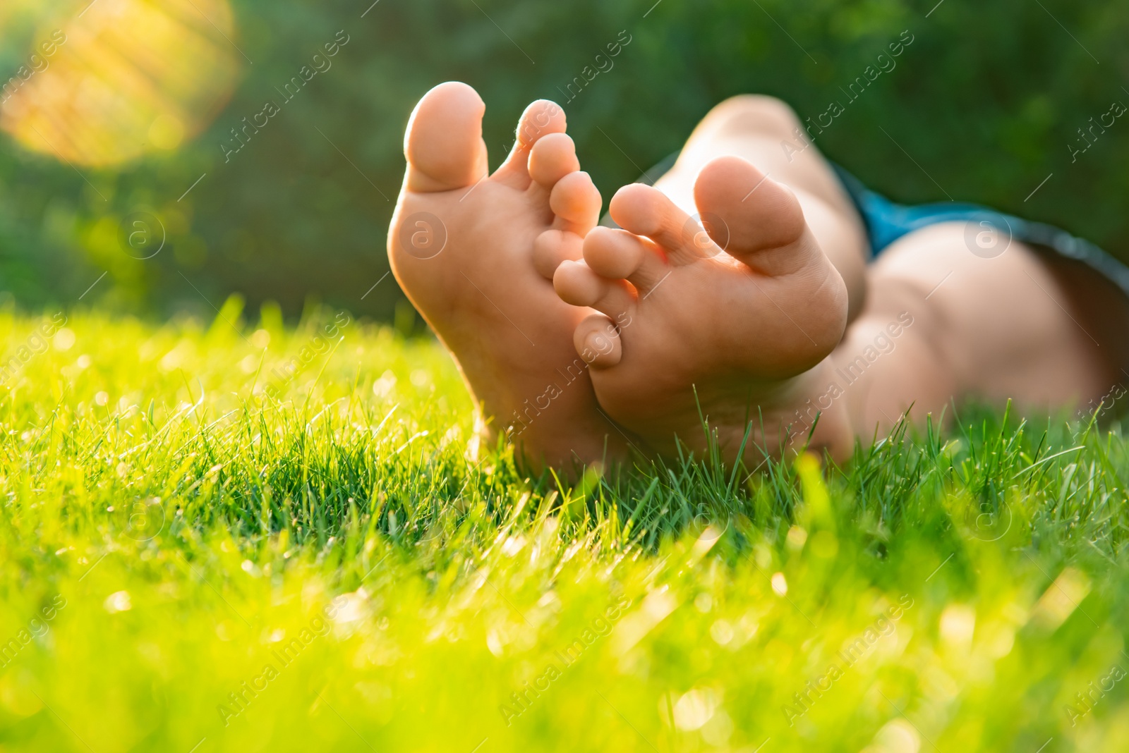 Photo of Teenage girl lying barefoot on green grass outdoors, closeup