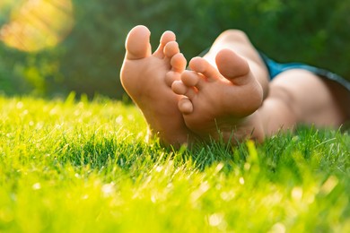 Photo of Teenage girl lying barefoot on green grass outdoors, closeup