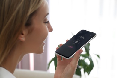 Photo of Young woman using voice search on smartphone indoors, closeup