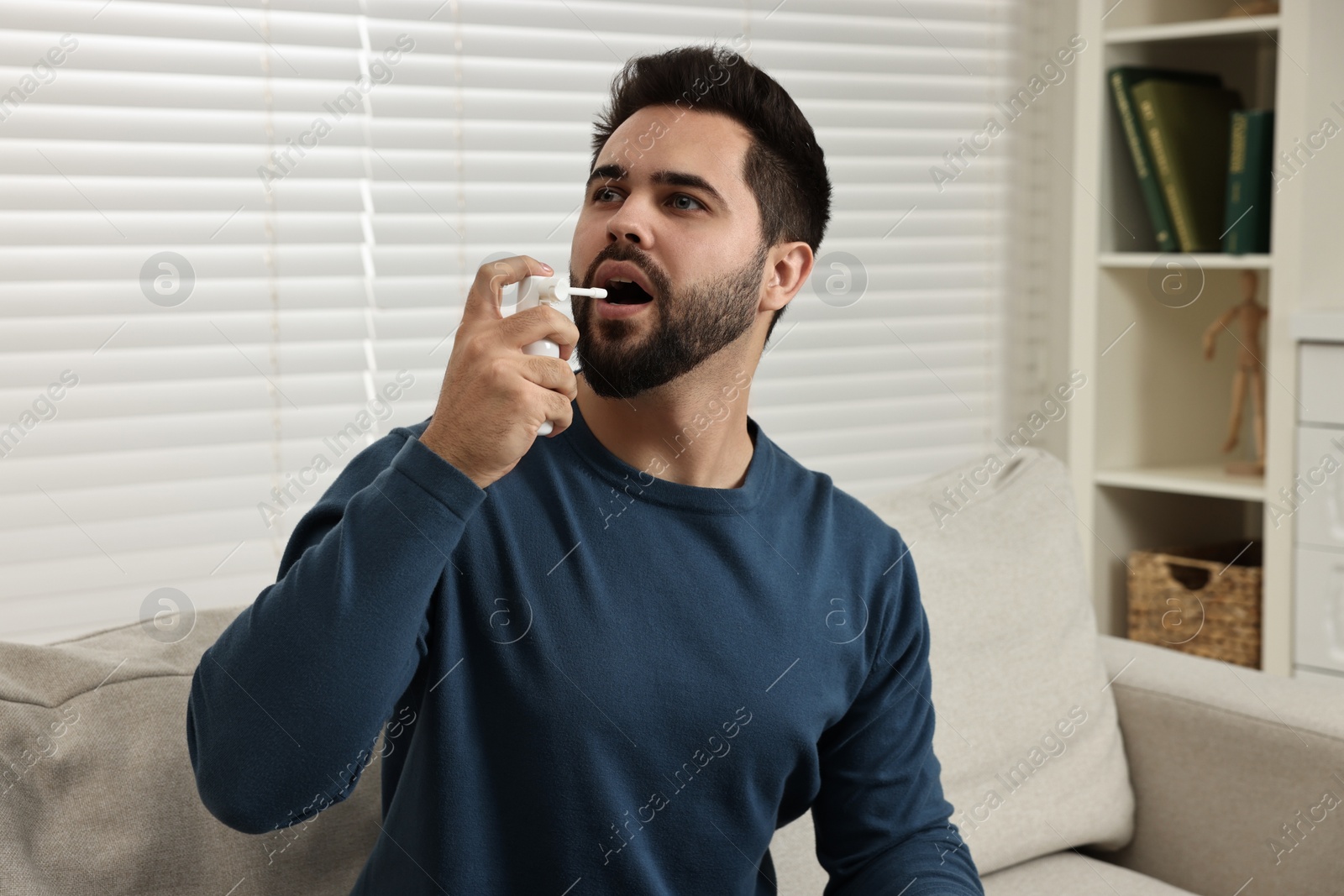 Photo of Young man using throat spray at home