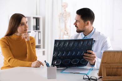 Orthopedist showing X-ray picture to patient at table in clinic