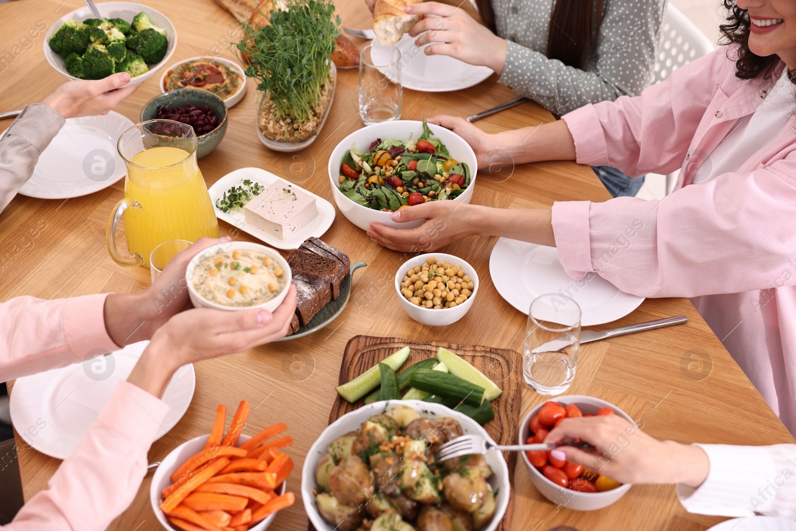 Photo of Friends eating vegetarian food at wooden table indoors, closeup