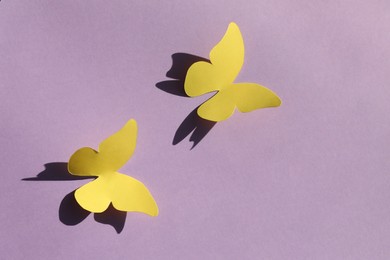 Photo of Yellow paper butterflies on violet background, top view. Space for text
