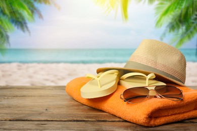 Image of Beach towel, flip flops, hat and sunglasses on wooden surface near seashore. Space for text 