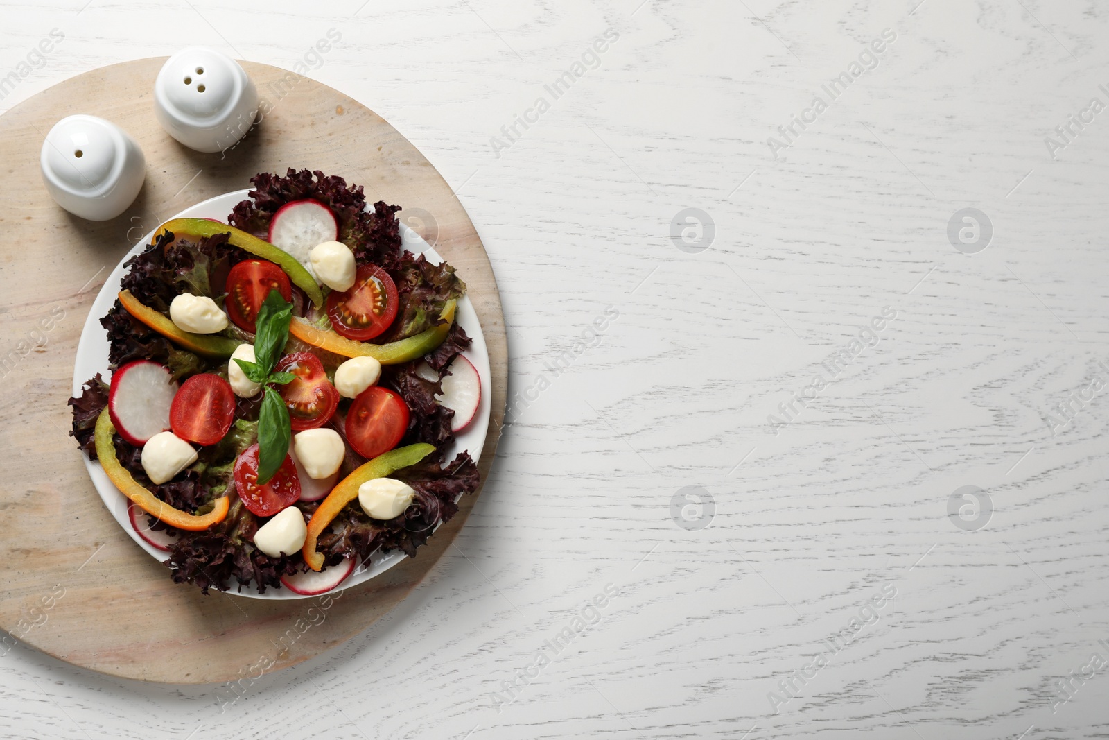 Photo of Delicious vegetable salad with mozzarella served on white wooden table, top view. Space for text
