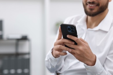 Young man using smartphone in office, closeup. Space for text