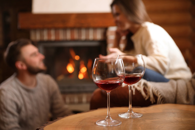 Photo of Lovely couple near fireplace at home, focus on glasses with wine. Winter vacation
