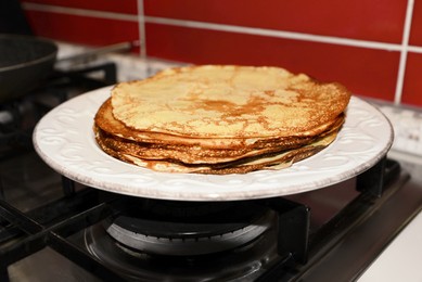 Photo of Plate of freshly made crepes on stove in kitchen, closeup