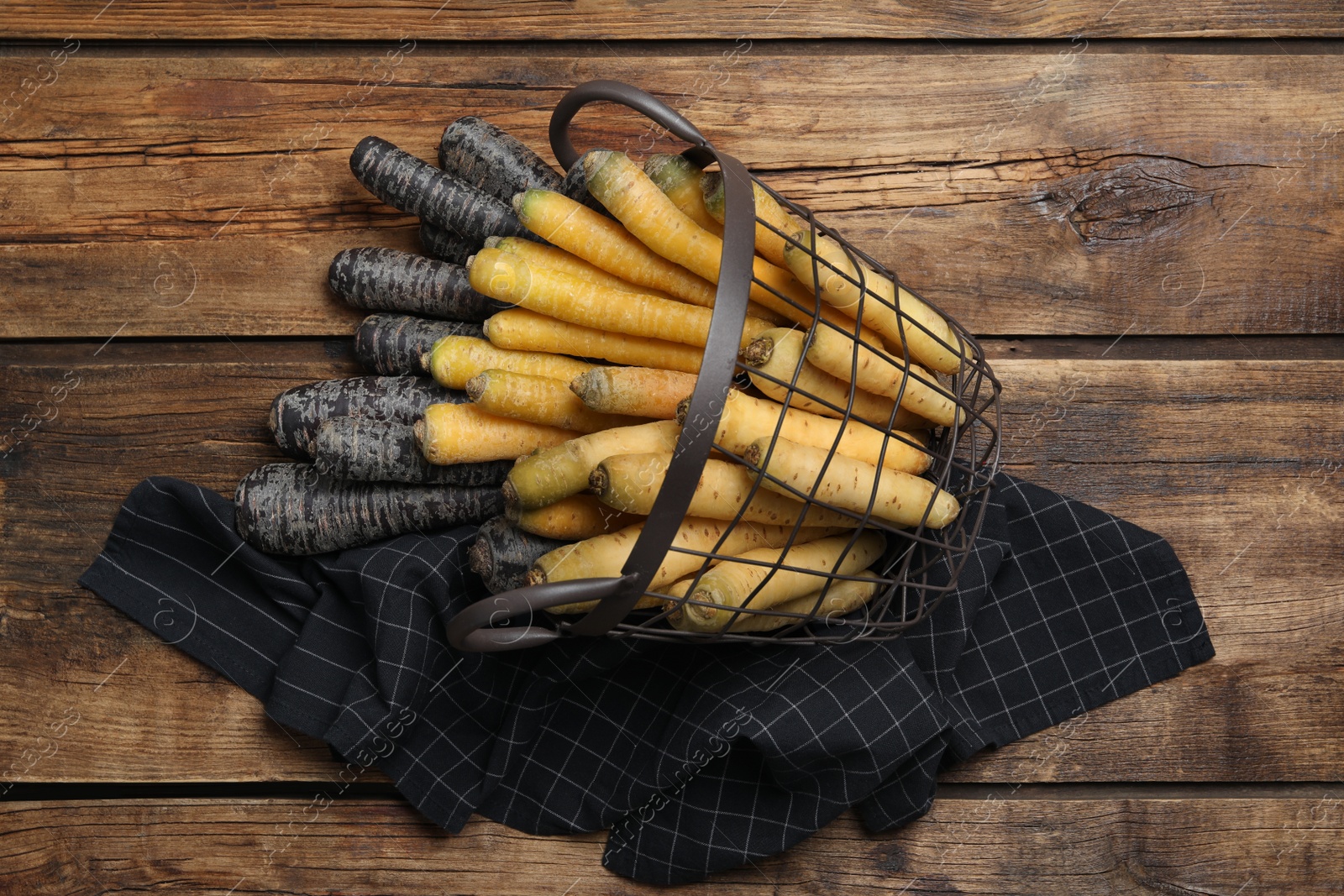 Photo of Many different raw carrots in metal basket on wooden table, flat lay