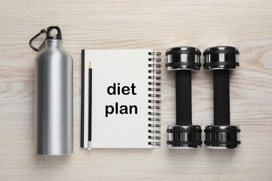 Weight loss concept. Flat lay composition with notebook, dumbbells and bottle of water on white wooden table