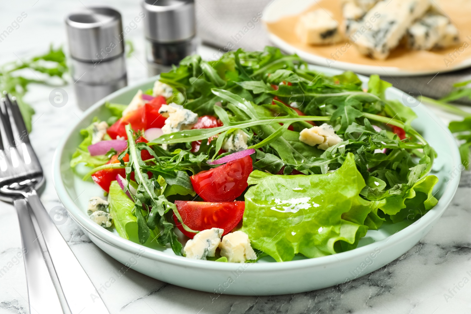 Photo of Delicious salad with arugula and tomatoes on white marble table, closeup