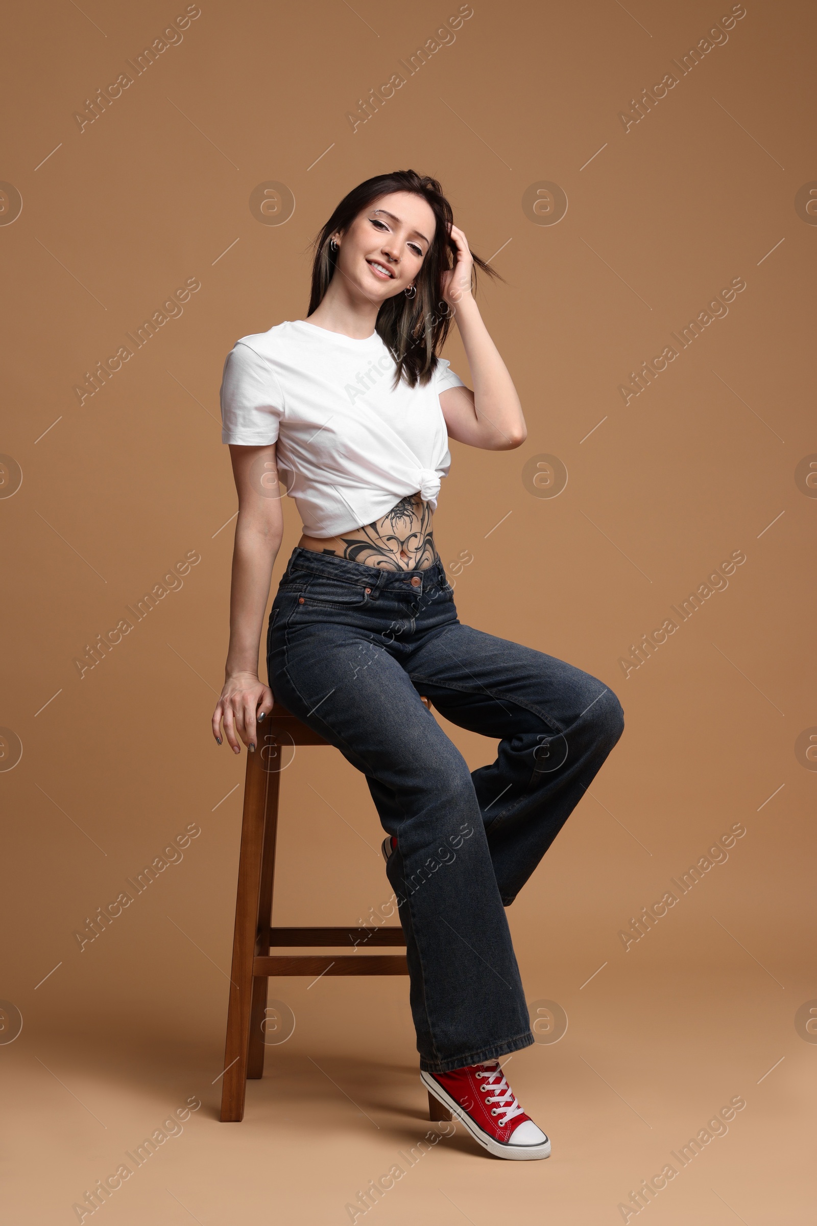 Photo of Smiling tattooed woman sitting on stool against beige background