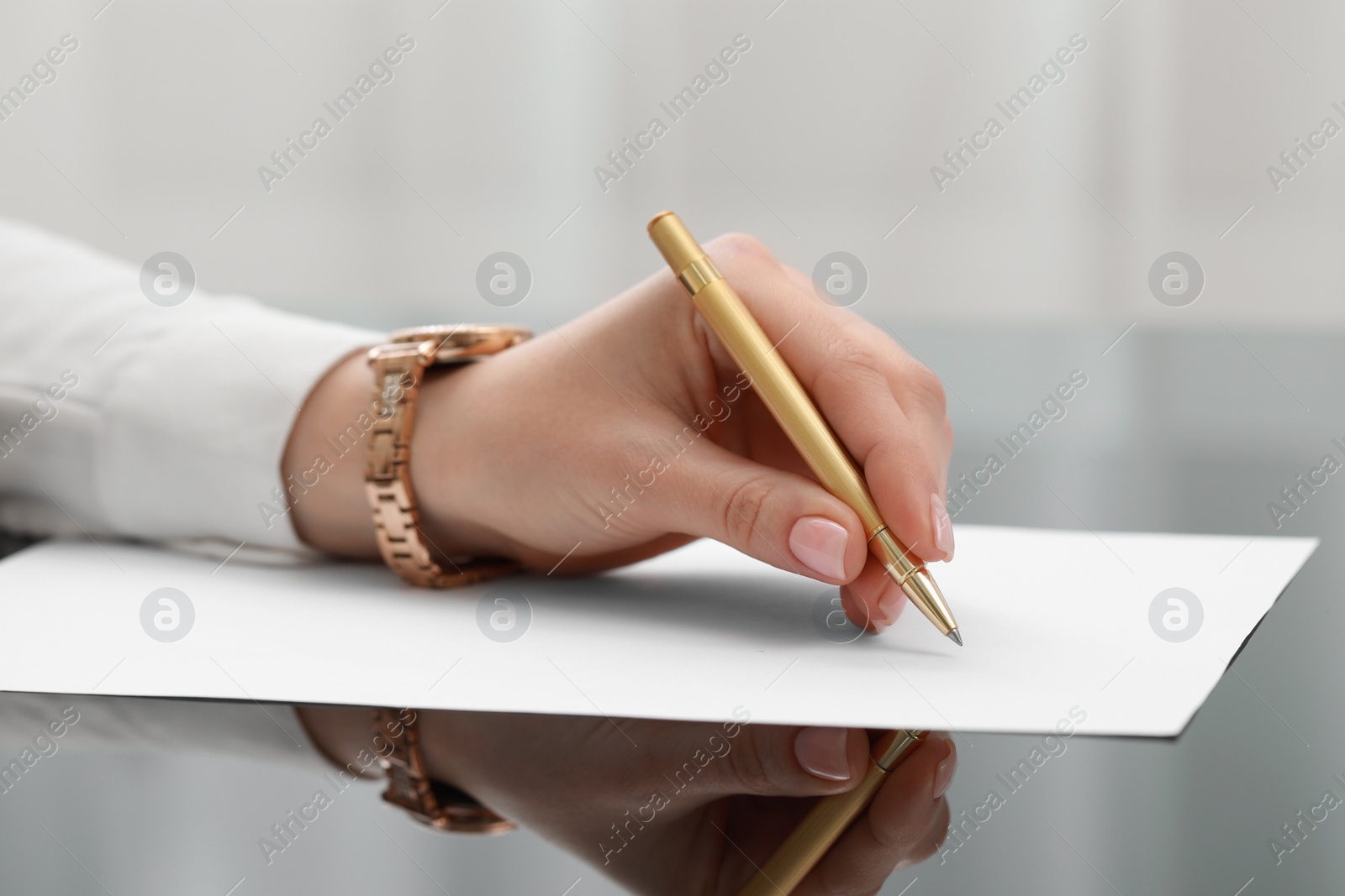 Photo of Woman writing on sheet of paper at glass table, closeup