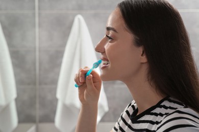 Young woman brushing her teeth with plastic toothbrush in bathroom
