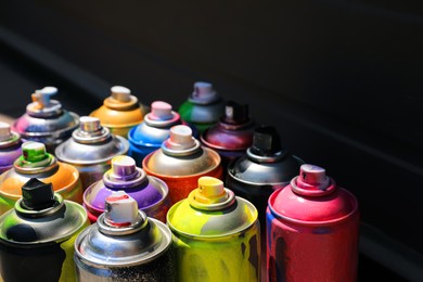 Photo of Used cans of spray paint on dark background, space for text. Graffiti supplies