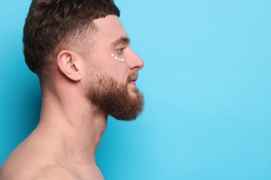 Photo of Handsome man with moisturizing cream on his face against light blue background, space for text