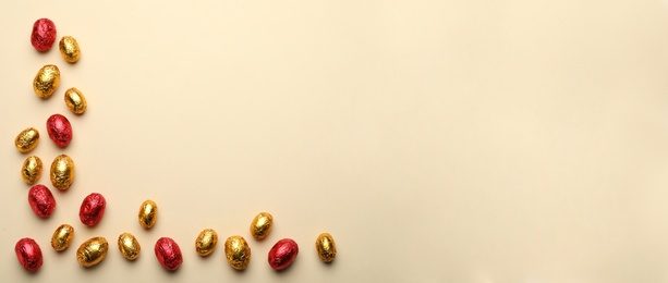 Chocolate eggs wrapped in red and golden foil on beige background, flat lay. Space for text