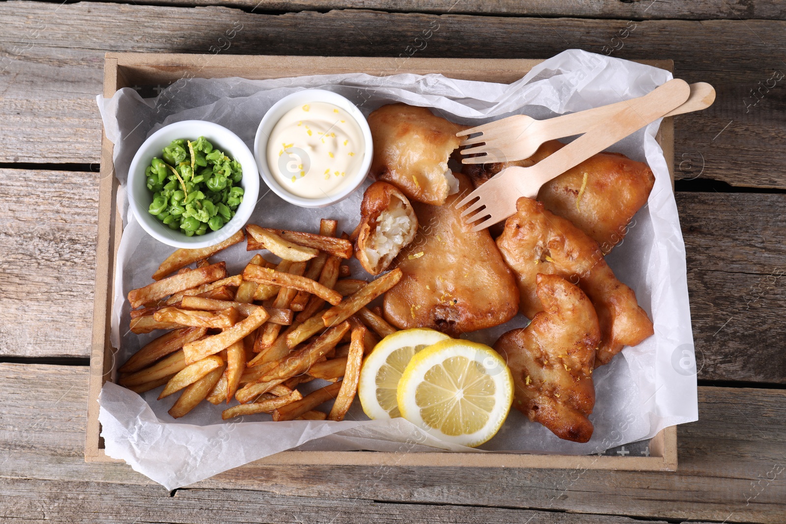 Photo of Tasty fish, chips, sauce and peas on wooden table, top view