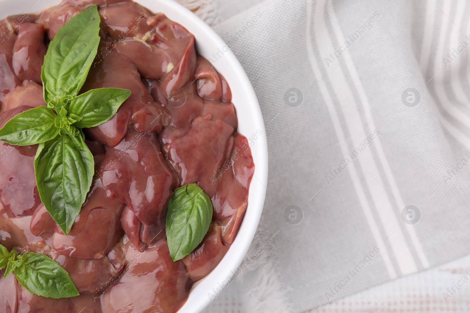 Photo of Bowl with raw chicken liver and basil on white table, top view. Space for text