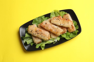 Photo of Tasty fried spring rolls and lettuce on yellow table, top view