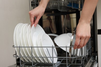 Photo of Woman loading dishwasher with plates indoors, closeup