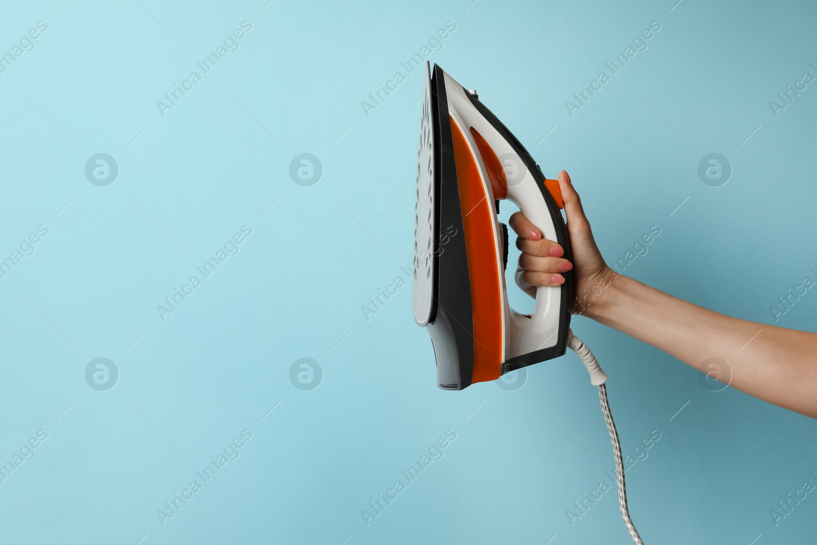 Photo of Woman holding modern iron on turquoise background, closeup. Space for text