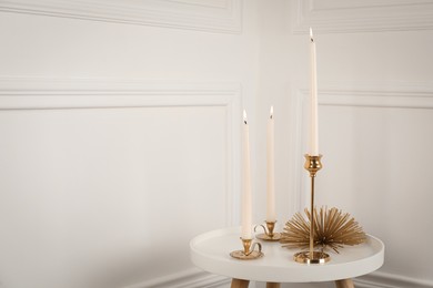 Elegant candlesticks with burning candles on white table. Space for text