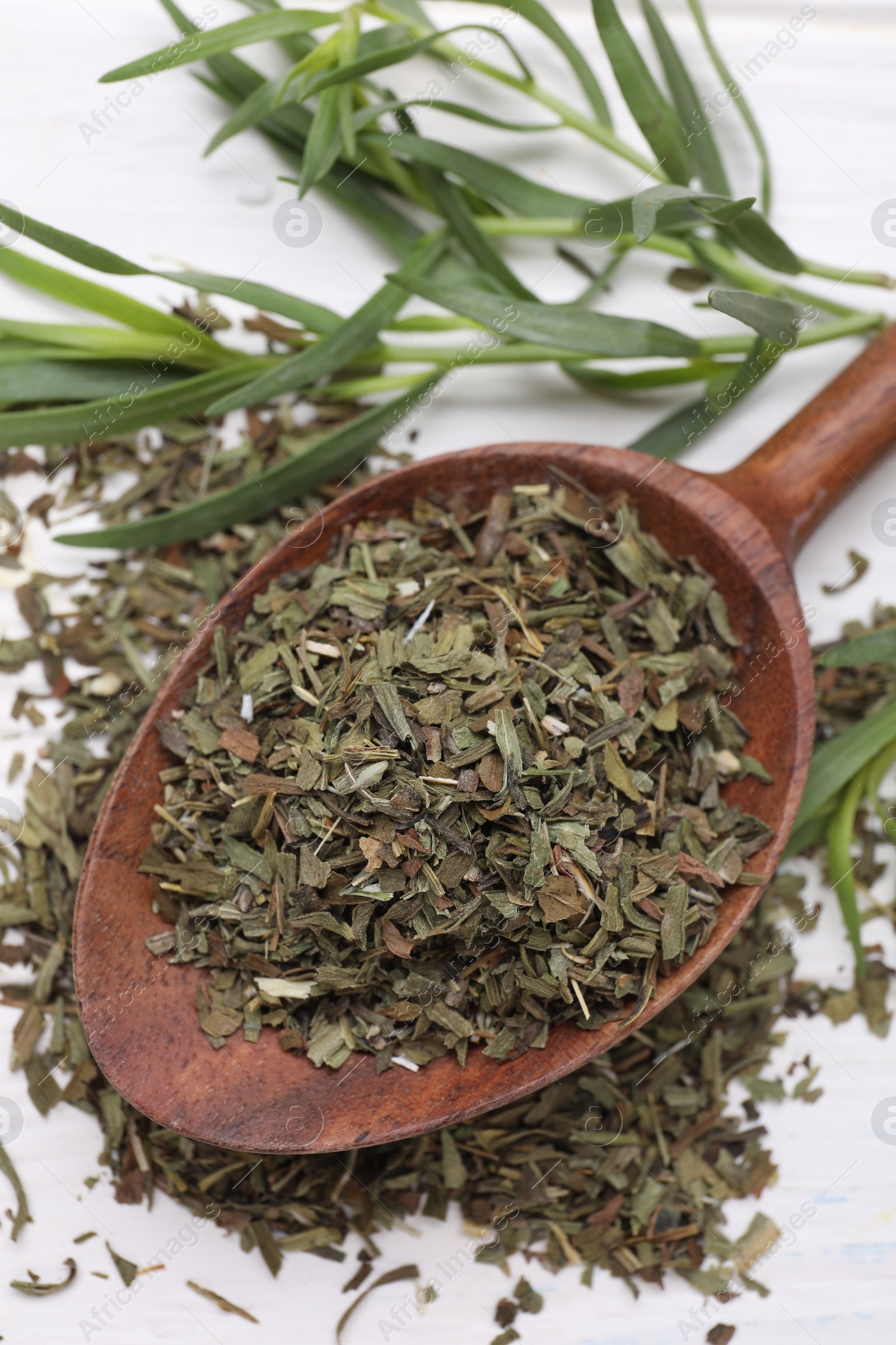 Photo of Spoon of dry tarragon and fresh leaves on white wooden table, above view