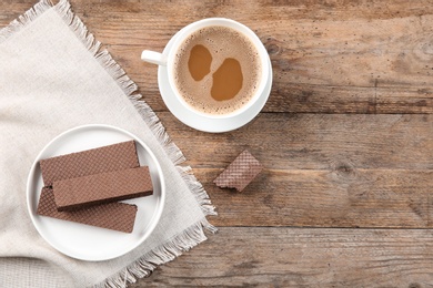 Plate of delicious chocolate wafers with cup of coffee on brown wooden background, top view. Space for text