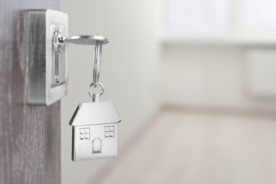 Mortgage and real estate. Open door with key and house shaped keychain against blurred background, space for text