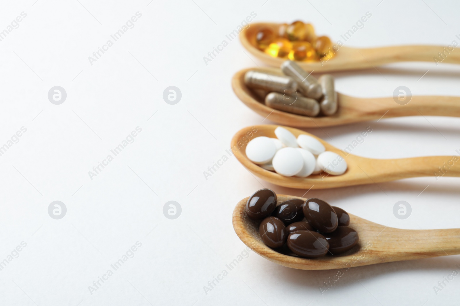 Photo of Wooden spoons with different dietary supplements on white background. Space for text