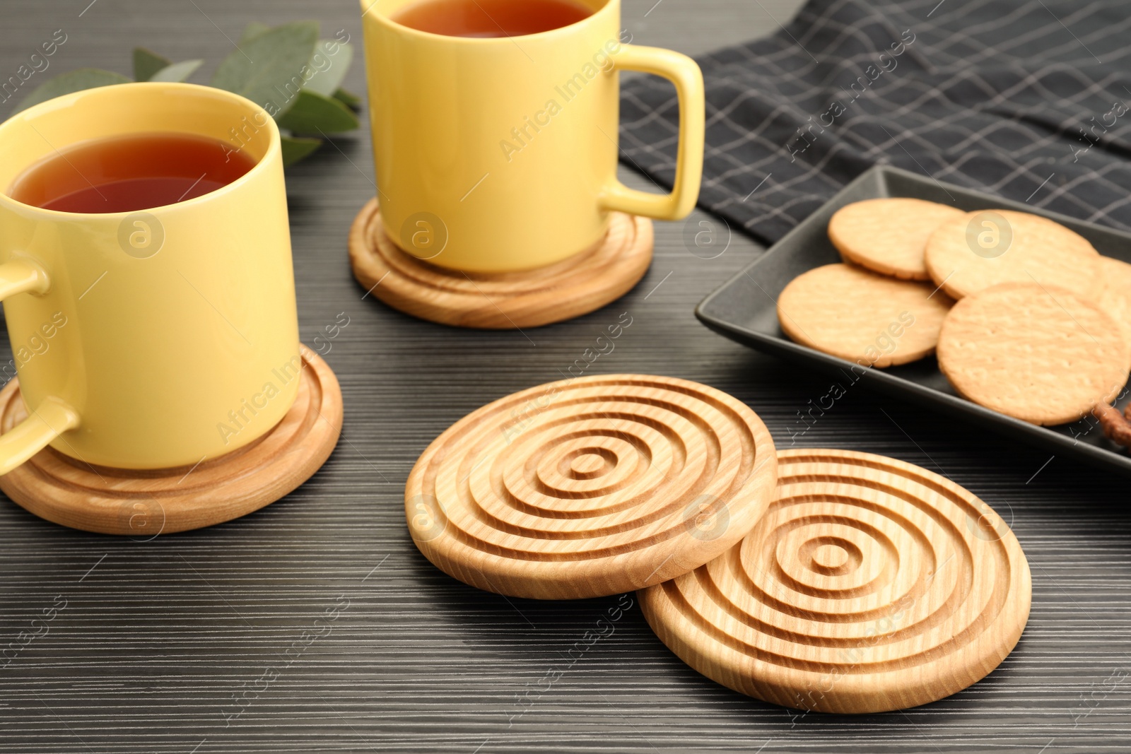 Photo of Stylish wooden cup coasters, mugs and cookies on black table