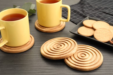 Stylish wooden cup coasters, mugs and cookies on black table