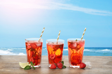 Tasty refreshing drink on wooden table against sea